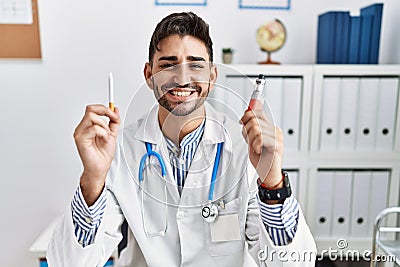 Young doctor man holding electronic cigarette at medical clinic smiling with a happy and cool smile on face Stock Photo