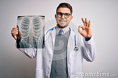 Young doctor man wearing medical coat looking at chest scan radiography over isolated background doing ok sign with fingers, Stock Photo