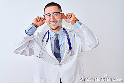Young doctor man wearing stethoscope over isolated background Smiling pulling ears with fingers, funny gesture Stock Photo
