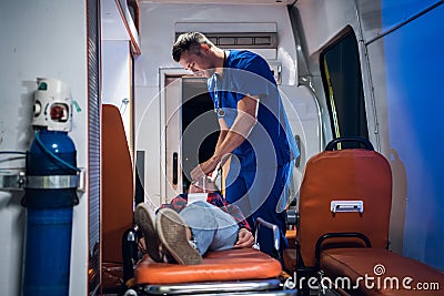 Doctor in medical uniform puts oxygen mask on woman lying on stretcher in the ambulance car Stock Photo