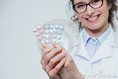 A young doctor doctor stands on a gray background isolated. During this, it holds three blister packs in its hands Stock Photo