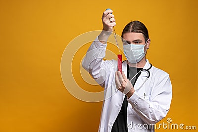 Young doctor using a pipette and a red tube, wearing protection mask and a stethoscope is trying to find a vaccine Stock Photo