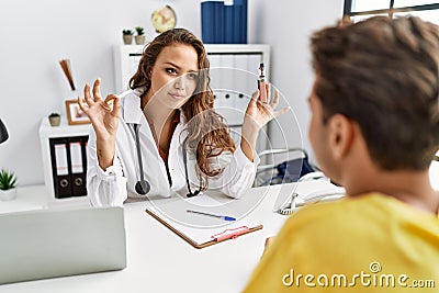 Young doctor woman showing electronic cigarette and normal cigarrete to patient relaxed with serious expression on face Stock Photo