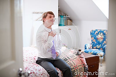 Young Downs Syndrome Man Sitting On Bed Getting Dressed For Work Stock Photo