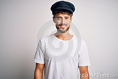 Young driver man with beard wearing hat standing over isolated white background with a happy and cool smile on face Stock Photo