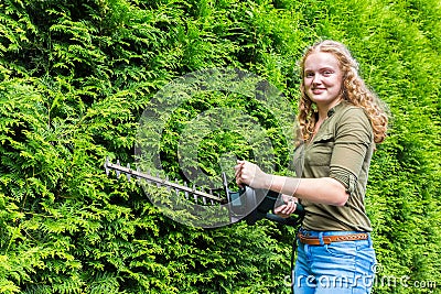 Young dutch woman holding hedge trimmer at conifers Stock Photo