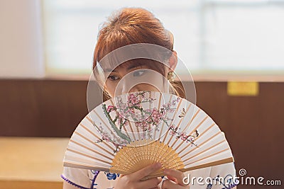 Young East Asian woman posing with an ornate oriental-style fan in front of her face. Stock Photo