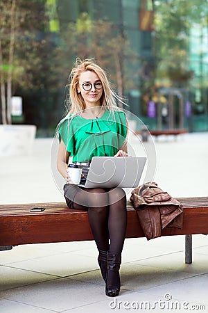 Young eastern European businesswoman walking on laptop on coffee break outside office building in windy day. Stock Photo