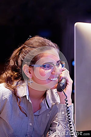 Young efficient secretary working in the office, she is answering phone calls. Customer service concept. Night time Stock Photo