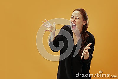 The young emotional angry woman screaming on gold studio background Stock Photo