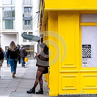 Young Ethnic Woman Leaning Against Yellow Building Using Mobile Phone Editorial Stock Photo