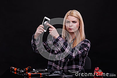 A girl, with a serious look, listens to a smartphone with a broken screen through a stethoscope. Stock Photo