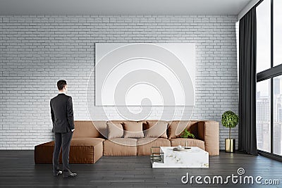 Young european businessman standing in modern living room interior with big couch, empty white mock up banner on brick wall, other Stock Photo