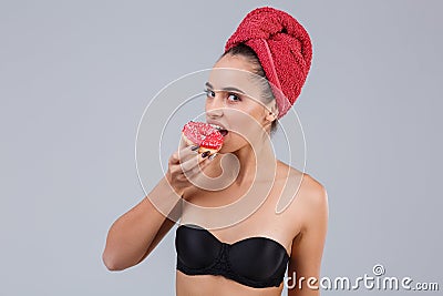 A young girl, in a black bra and with a red towel on her head, bites a donut with sugar glaze. Stock Photo