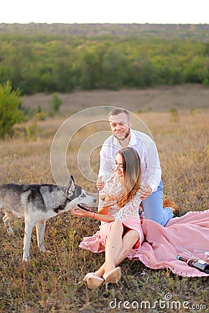 Young european girl and boy sitting on pink plaid near husky and resting. Stock Photo