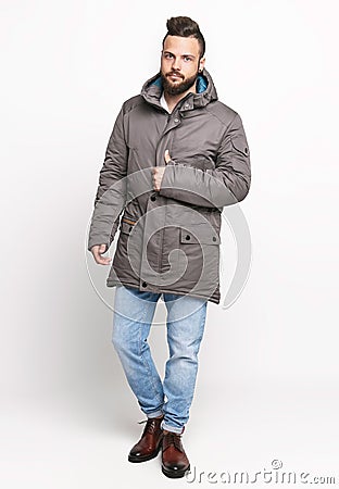 Young European man in white sweater and blue jeans, gray down jacket posing on a white background. Photo concept for advertising a Stock Photo