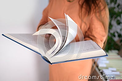 Young european woman with long hair holds a thick book in a blue cover in her hands, flips through the pages, concept of fiction, Stock Photo