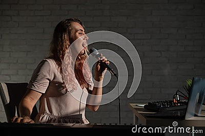 A young European woman sings into a microphone and accompanies on an electronic piano. The girl shoots a video blog Stock Photo