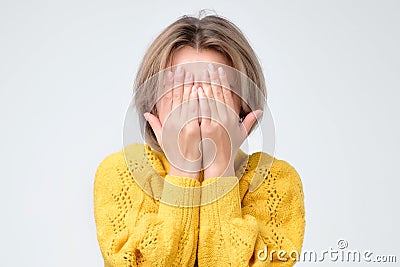 Young european woman in yellow sweater hides her face Stock Photo