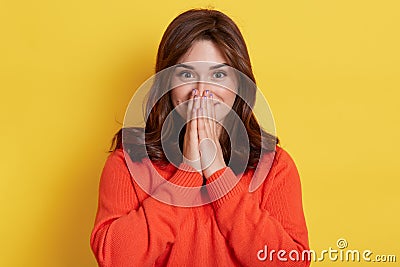 Young excited happy surprised wondered beautiful woman wearing casual orange sweater, covering mouth with hand, looking at camera Stock Photo