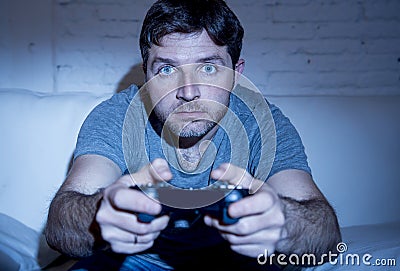 Young excited man at home sitting on living room sofa playing video games using remote control joystick Stock Photo