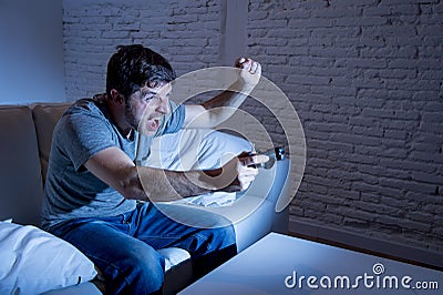 Young excited man at home sitting on living room sofa playing video games using remote control joystick Stock Photo