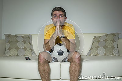 Young excited and nervous football supporter man watching soccer game on television at living room sofa feeling emotion and stress Stock Photo
