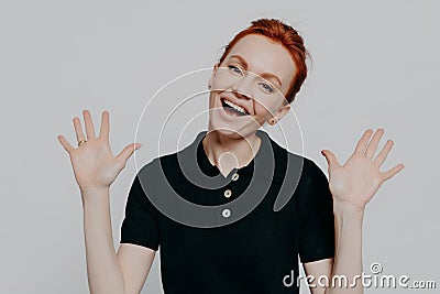 Young excited red haired woman raising palms and exclaiming loudly, isolated over grey background Stock Photo
