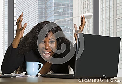 Young exhausted and depressed black African American business woman working upset and sad at office computer desk by the window in Stock Photo