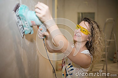 Young fair-haired curly woman makes repairs in the dwelling with construction tools. Stock Photo