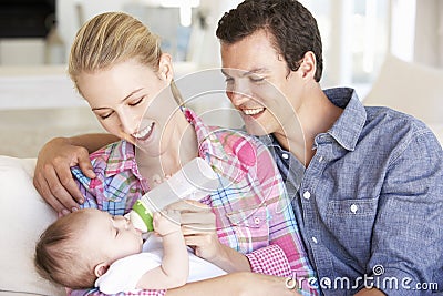 Young Family With Baby Feeding On Sofa At Home Stock Photo