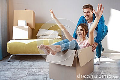 Young family couple bought or rented their first small apartment. Cheerful happy people having fun. She sit in box and Stock Photo