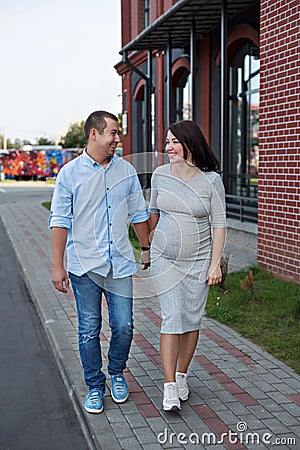Family couple men and a young pregnant woman walking holding hands and laughing along the city windows Stock Photo