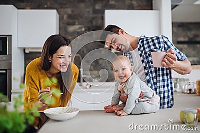 A young family at home, a man holding a baby and a woman feeding her. Stock Photo