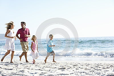 Young Family Running Along Sandy Beach On Holiday Stock Photo