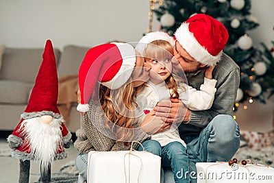 Young family in santa claus hat. Parents kiss their daughter. Stock Photo