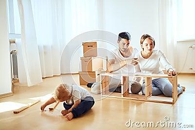 Family together at living room of new apartment assembling furniture, pile of moving boxes on background Stock Photo