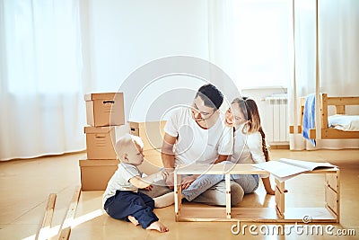 Family together at living room of new apartment assembling furniture, pile of moving boxes on background Stock Photo