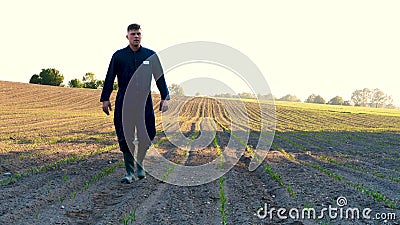 A young farmer in a blue robe walks the field looking at planted plants. Concept: clean air, bio, agriculture Stock Photo