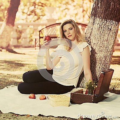 Young fashion blonde woman with apple in city park Stock Photo