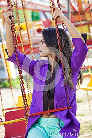 Young fashion caucasian brunette woman portrait sit on flying carousel in amusement park summer Stock Photo
