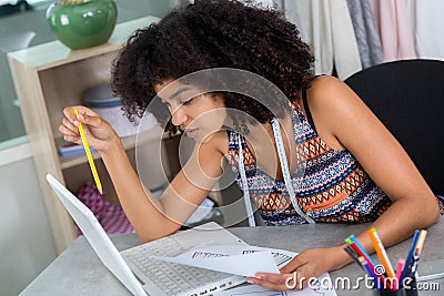 Young fashion designer looking at laptop and holding drawingn Stock Photo