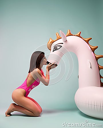 Young fashion woman kissing big inflatable unicorn pegasus float mattress in pink bikini for swimming pool Stock Photo