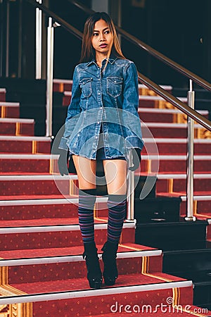 Young fashionable woman in blue jeans, and long striped knee socks walking down on stairs with the red carpet Stock Photo