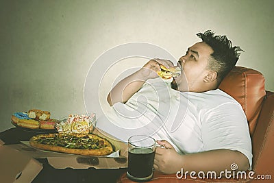 Young fat man eats burger with gluttony expression Stock Photo