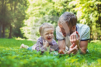 Young father and his son eating strawberries in Park. Picnic. Outdoor portrait Stock Photo