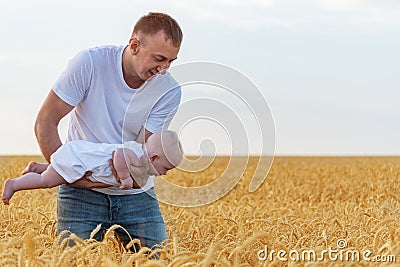 Young father playing with baby. Child flies over field in dads hands. Ripe wheat field Stock Photo