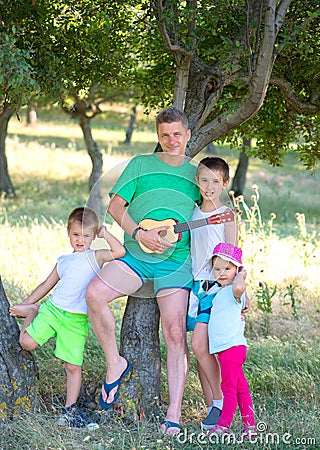 Young father plays the guitar for his young children in the forest Stock Photo