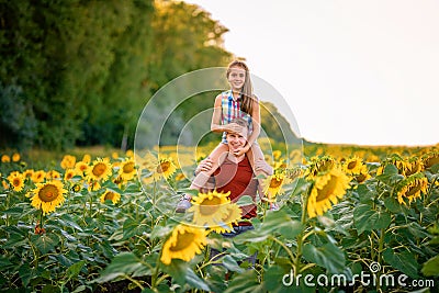 A young father plays with his daughter in a field of sunflowers. A little girl sits on her father`s neck and laughs. Family summer Stock Photo