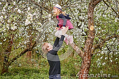 A young father plays with his daughter in a flowering garden. Throws up. Against the background of green grass and flowering trees Stock Photo